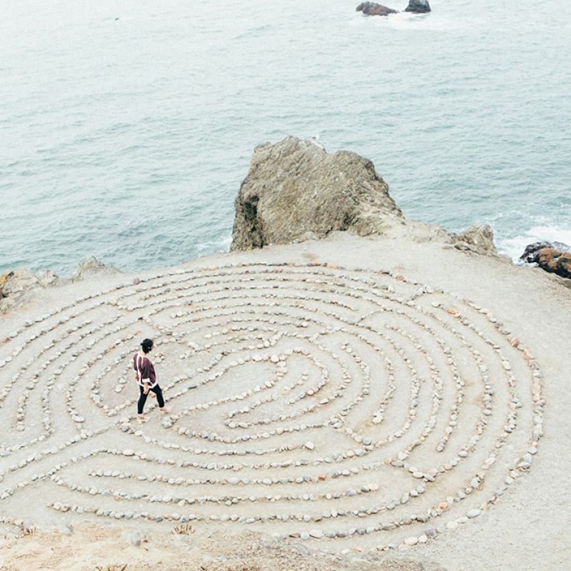 Person geht achtsam durch ein Steinkreis-Labyrinth am Meer – Sinnbild für innere Klarheit und persönliche Entwicklung.